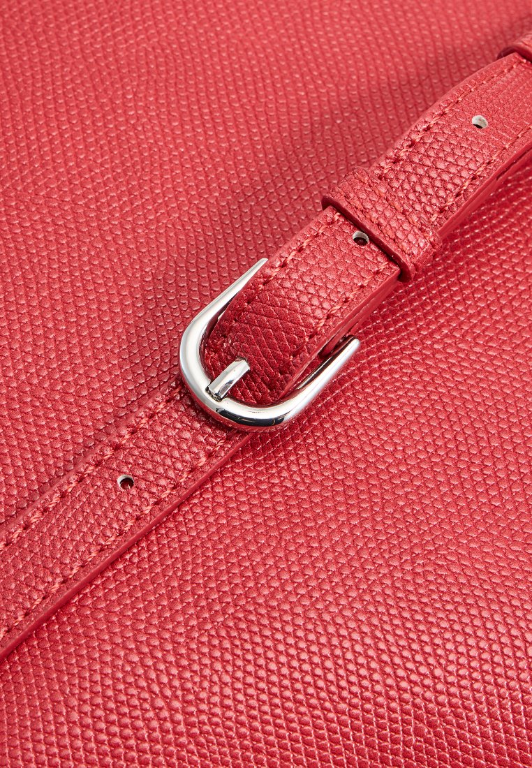 Rote, strukturierte Lederhandtasche mit einer Schnalle und einem Riemen aus silbernem Metall. Eine Nahaufnahme zeigt feine, geprägt Details und Nähte entlang der Kanten.