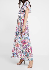 Maxikjole med et farverigt blomstermønster på en lys baggrund, korte flæser påærmer og en tætsiddende liv med en svævende nederdel.