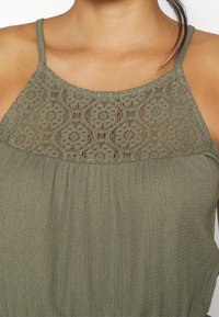 Olivově zelený top bez rukávů s krajkovým zakončením, s textured tkaninou a jemnými plisovanými detaily provolný střih.
