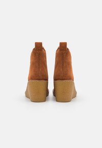 Pair of brown suede ankle boots with high textured wedge heels, viewed from the back on a white background.