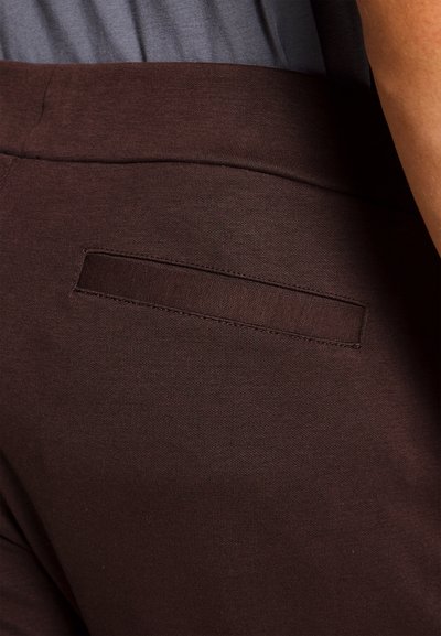 Calças de tecido elástico castanhas com um bolso traseiro liso e uma cintura suave, apresentando um design limpo e ajustado.