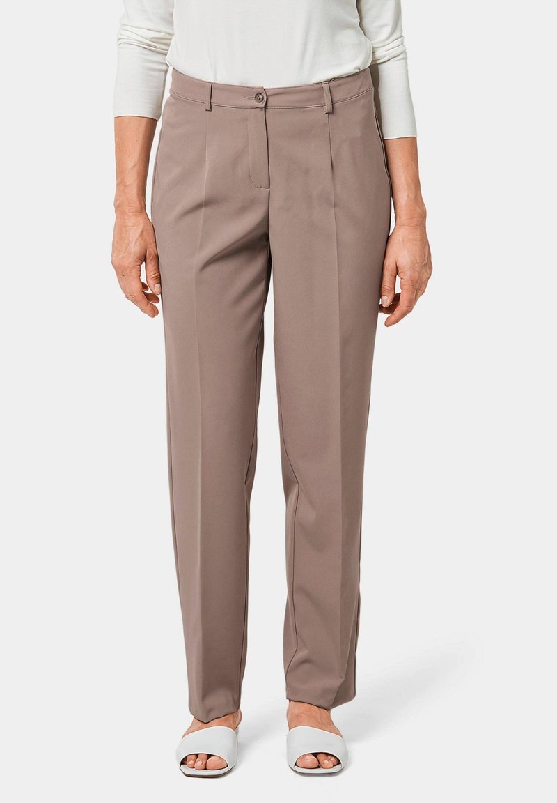 Beige op maat gemaakte broeken met een rechte pijp, knoopsluiting en voorplooien. Draagt met witte slide sandalen, die een gladde textuur tonen.