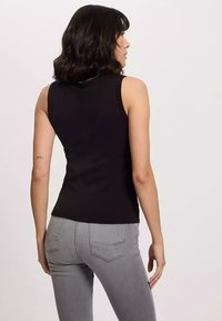 Czarny bezrękawnik o dopasowanym fasonie, wykonany z gładkiego materiału. Noszony z jasnoszarymi spodniami z tylnymi kieszeniami i klasycznym krojem.