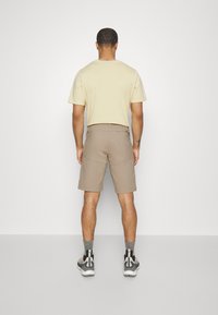 T-shirt beige, shorts marron clair et baskets noires avec des accents gris. Tissu en coton, coupe décontractée et détail de poche à l'arrière des shorts.