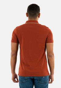 Polo a maniche corte di colore ruggine, realizzato in tessuto testurizzato con colletto a costine e rifiniture a contrasto lungo il collo.