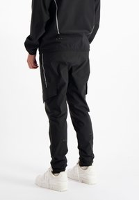 Zwarte cargobroek met een slim fit, gemaakt van lichtgewicht materiaal, met zijzakken en reflecterende accenten, gecombineerd met witte sneakers.