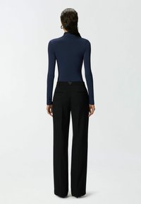 Mornarska bodi majica s dugim rukavima elegantnog dizajna, u kombinaciji s crnim hlačama visokog struka koje imaju dva stražnja džepa i suptilni trokutasti detalj.