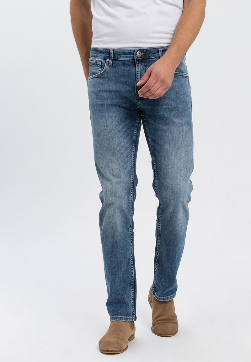 Lichtblauwe denim jeans met een rechte pijp, vijf zakken en subtiele vervaging. Gecombineerd met tan, enkellaarsjes.