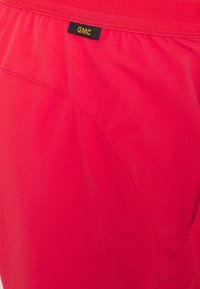 Shorts de un brillante color rosa, hechos de un tejido suave con una textura lisa, que presentan una etiqueta negra de QMC y un sutil detalle en las costuras.
