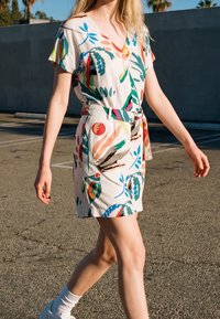 Femme marchant dehors portant une robe à manches courtes ceinturée avec des motifs floraux abstraits colorés et des baskets blanches avec des chaussettes.