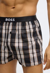 Fekete boxeralsó barna, szürke és fehér kockás mintával. Fekete elasztikus derékpánttal, rajta a "BOSS" logóval, és gombos sliccel.