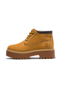 Tan leren enkelboots met een ronde neus, bruine accenten, een dikke plateauzool en contrasterende gele veters. Heeft een logo aan de zijkant.