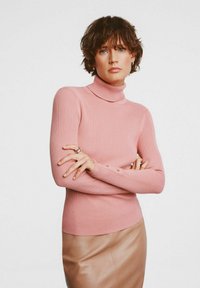 Jasnoróżowy sweter typu turtleneck z prążkowanym wzorem, z dopasowanymi rękawami, ozdobiony guzikami na mankietach. Noszony na skórzaną spódnicę w kolorze brązowym.