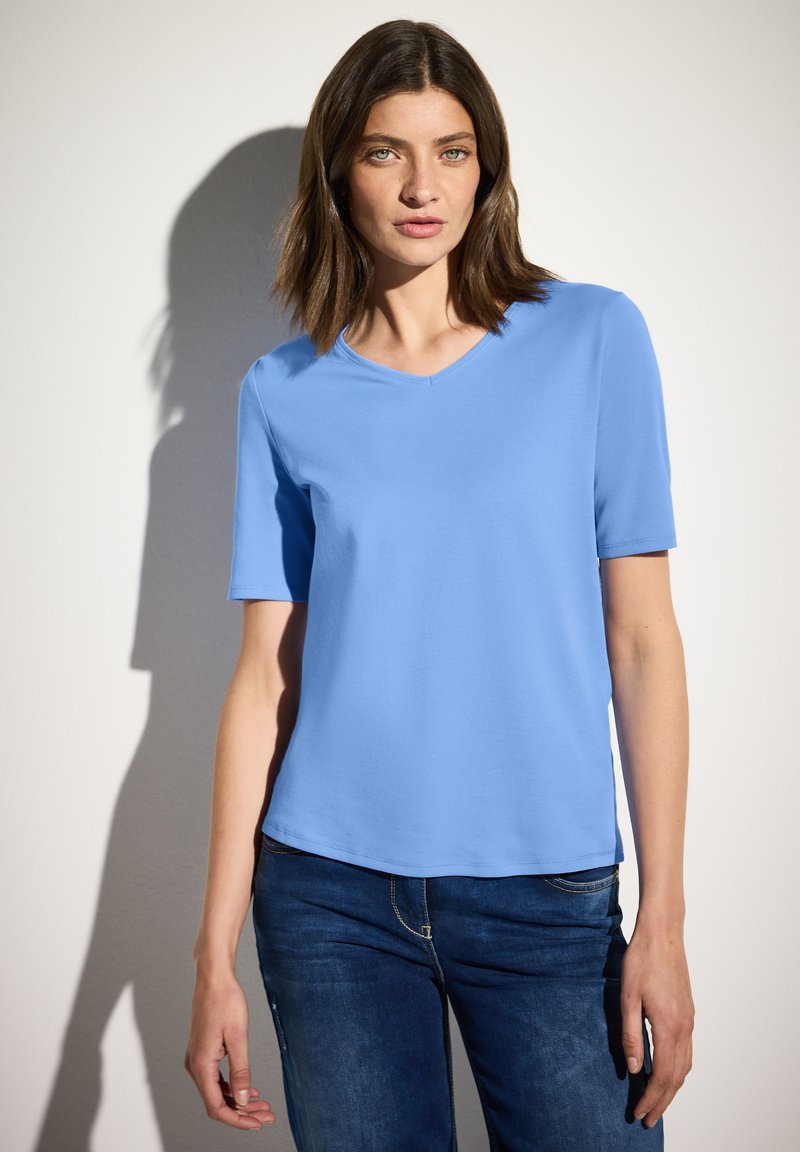 Světle modré tričko s krátkým rukávem a výstřihem do V vyrobené z hladké, elastické látky, spárované s tmavě modrými džíny s jemnými prošitými detaily.