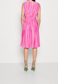 Sukienka bez rękawów, do kolan, w jasnoróżowym plisowanym materiale, z wycięciem na plecach i elastycznym pasem. W zestawie z zielonymi sandałami na obcasie.