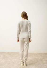 Pull en ribbed gris clair avec des manches longues, associé à un pantalon tapered beige doux et une paire de baskets épaisses. Texture lisse, design minimaliste.