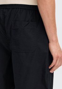 Mustad lühikesed püksid, valmistatud kerge kangaga, millel on küljetasku ja elastne vöökoht mugavuse tagamiseks. Sile tekstuur, vabaaja disain.