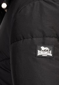 Must must jacket, mille tekstuuriga viimistlusega ja silmapaistva Lonsdale'i logoga varrukal. Sisaldab nööbikinnitust kaeluses.