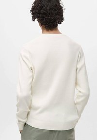 Pull en crème clair à côtes avec un col rond et des poignets ajustés. Texture douce, design sans coutures et coupe légèrement ajustée à la taille.