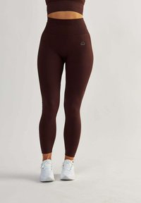 Burgundské legíny s vysokým pasem, s ribbovanou texturou a hladkým povrchem. Malý detail srdíčka na přední straně, doplněné bílými sportovními botami.