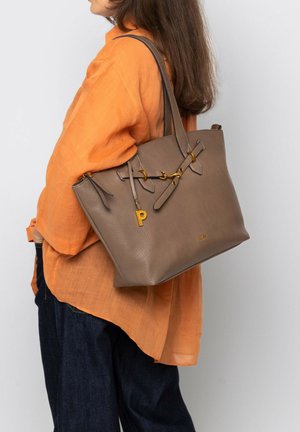 Graue Ledertasche mit strukturierten Oberflächen, goldfarbenen Hardware-Akzenten und einem abnehmbaren Charm. Trägt man über einer orangefarbenen Bluse.