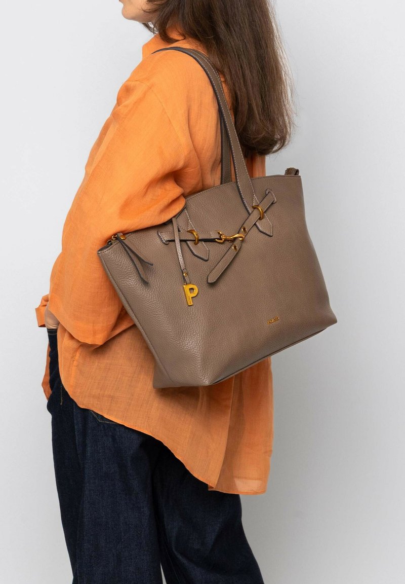 Sac fourre-tout en cuir gris avec une surface texturée, des accents en métal doré et un charme détachable. Porté sur un blouse orange.