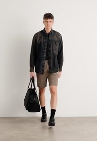 Chemise en denim noir, shorts beige, chaussures noires, portant un sac tote noir. Design à coupe droite, fermeture à bouton, et texture subtile sur la chemise.