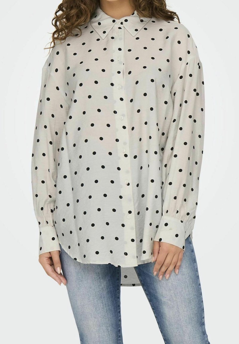 Long-sleeve button-up shirt in light cream with black polka dots. Features a classic collar and cuffed sleeves, made from a lightweight fabric.