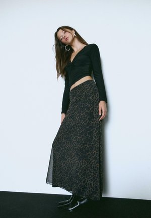 Top nero a maniche lunghe con davanti intrecciato, abbinato a una gonna maxi con stampa leopardata in toni scuri, completato con stivali neri alla caviglia.
