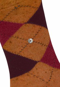 Zbliżenie brązowej, burgundowej i pomarańczowej tkaniny w wzór argyle z małym, okrągłym metalowym guzikiem na środku.