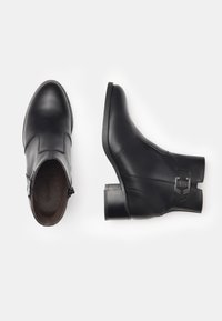 Schwarze Leder-Stiefeletten mit glatter Oberfläche, runder Zehenpartie und niedrigem Blockabsatz. Ausgestattet mit einem seitlichen Reißverschluss und einem dekorativen Schnallen-Detail.