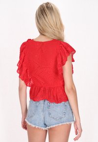 Rød broderet bluse med flæser på ærmerne og peplum-skjorte. Kombineret med lyse denimshorts med frynser og baglommer.