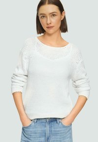 Witte gebreide trui met een losse pasvorm, ronde halslijn en driekwart mouwen. Gekozen boven lichtblauwe jeans. Gestructureerde stof met open stiksels.