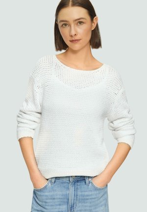 Weißer Strickpullover mit lockerer Passform, rundem Halsausschnitt und Dreiviertelärmeln. Getragen über hellblauen Jeans. Strukturierter Stoff mit offenen Nähten.