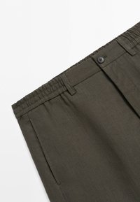 Mörkgröna byxor med elastisk midja, knapp och bältesöglor, med sidofickor och en slät tygstruktur.