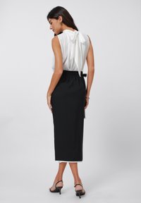 Blusa senza maniche bianca con dettagli a fiocco sul retro, abbinata a una gonna nera a vita alta con elastico in vita.