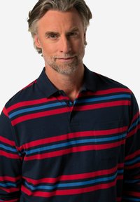 Námornická polo košile s dlouhým rukávem, přičemž má červené a modré vodorovné pruhy, tříknoflíkovou légu a kapsu na hrudi. Měkký bavlněný materiál.