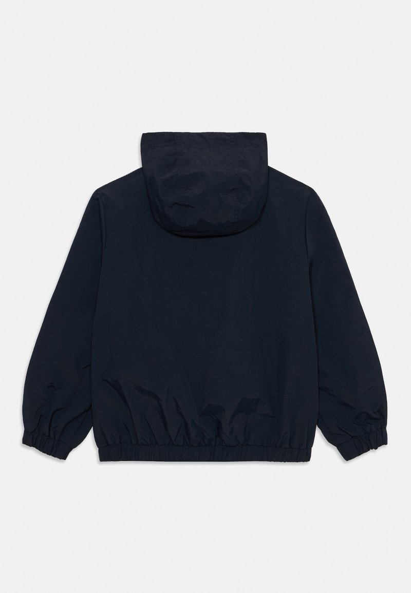 Veste coupe-vent bleu marine en tissu lisse et léger ; dotée d'une capuche et de poignets élastiques, avec un ourlet froncé pour un ajustement décontracté.