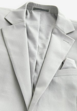 Blazer gris claro con un tejido texturizado, solapas de muesca, un pañuelo en el bolsillo y un forro estampado. Presenta detalles de costura minimalistas.