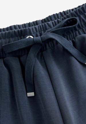 Marineblaue Hosen aus glattem Stoff mit einem elastischen Bund und einem flachen Kordelzug, die am Ende eine metallische Akzentuierung haben.