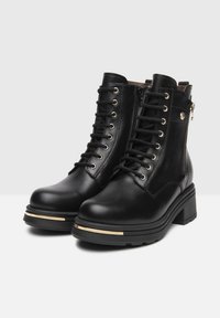 Zwarte leren enkelboots met vetersluiting aan de voorkant, zijrits, goudaccenten op de zool en stevige blokhak. Glad oppervlak en casual ontwerp.
