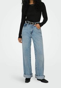 Ljust blå vida jeans med uppvikt nederkant, hög midja och klassisk femfickdesign. Matchas med en kroppsnära svart långärmad topp.