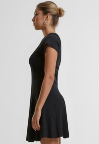 Robe noire à manches courtes avec un corsage ajusté et une jupe évasée. Fabriquée en tissu côtelé, mettant en valeur une texture lisse et un mouvement subtil.
