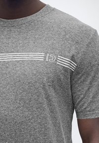 Close-up af en person iført en gråmeleret t-shirt med et hvidt stribet design og delvist synlig "G1" tekst over brystet.