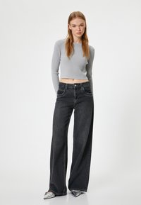 Grijze geribbelde cropped trui gecombineerd met high-waisted, wijdvallende zwarte jeans, met voorzakken en een klassieke knoopsluiting.