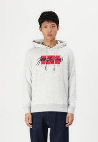 Sudadera gris claro con un bolsillo frontal, que presenta un estampado gráfico en rojo y azul marino. Los cordones y los puños acanalados completan el diseño.