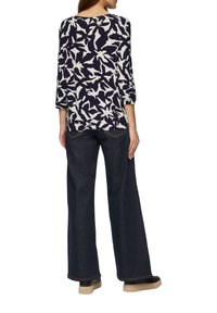 Navyblaues Oberteil mit weißem abstraktem Blumenmuster, Dreiviertelärmel, kombiniert mit dunkelblauen weit geschnittenen Jeans und schwarzen Schuhen mit strukturiierter Sohle.