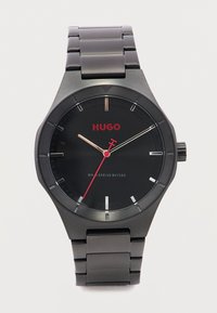 Μαύρο μεταλλικό ρολόι χειρός με κόκκινο δευτερόλεπτο δείκτη, λογότυπο Hugo και αντοχή στο νερό έως 50 μέτρα σε σύνδεστη μπρασελέ.