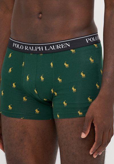 Zelena bokserska kratka hlača iz bombaža, ki prikazuje ponovljen vzorec rumenega logotipa polo igralca, z črnim pasom z napisom "POLO RALPH LAUREN."