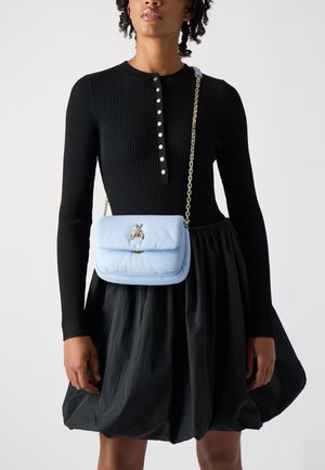 Borsa a tracolla in pelle blu chiaro con un emblema d'argento a forma di ape, dotata di una tracolla a catena e di una morbida texture trapuntata. Indossata sopra un vestito nero.